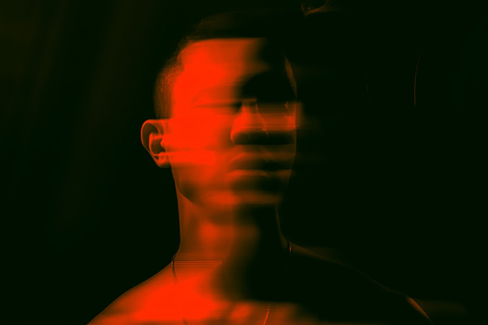 A red-tinted double-exposure portrait of a person’s face, blurred and fractured as if pulled in two directions at once