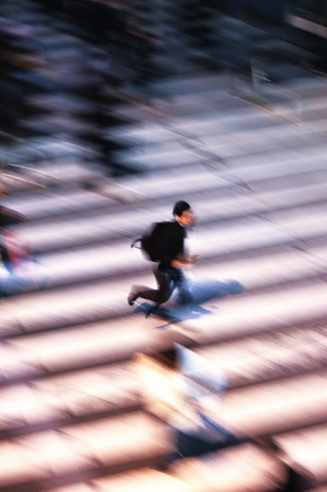 Motion-blurred figure moving quickly across a crosswalk, evoking constant busyness